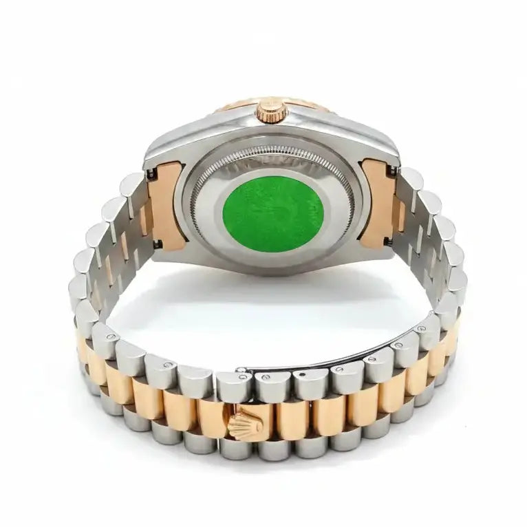 The back of a two-tone stainless steel and gold watch with a metal link bracelet, featuring a green circular insert on the case back.
