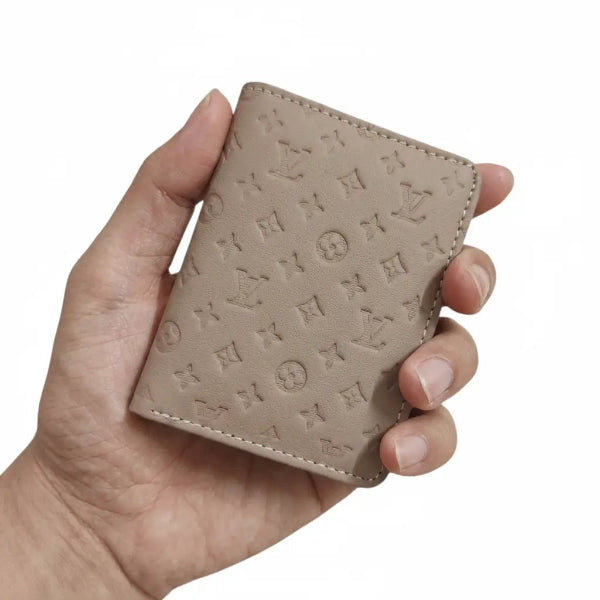 Hand holding a beige embossed wallet with a brand logo on a white background