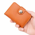 Hand holding a brown leather wallet with a gold button on a white background