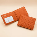 An orange-brown leather bi-fold wallet shown open and closed on a warm beige background. The closed wallet displays an embossed monogram pattern, and the open wallet reveals card slots and a clear ID window.