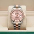 Rolex Oyster Perpetual watch with a pink dial, diamond-set bezel, and a two-tone stainless steel and rose gold bracelet, displayed on a cream cushion inside its box.