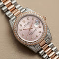 Rolex Datejust wristwatch with a two-tone rose gold and stainless steel Oyster Perpetual bracelet, a pink dial, and a diamond-set bezel on a beige textured background.