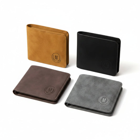 Four bifold wallets in brown, tan, black, and gray suede-like finishes arranged on a wooden desk, each with an embossed circular monogram 'M' on the front. Pens and notebooks are visible in the background.