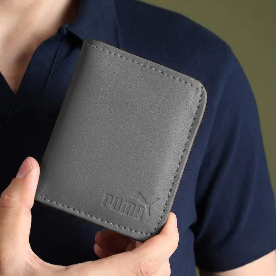 A person holding a dark gray Puma bifold wallet against their navy blue polo shirt.