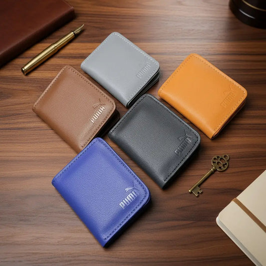 Five small bifold wallets in different colors are arranged on a wooden desk: brown, light gray, orange, black, and blue. Each wallet has a debossed logo on the front.